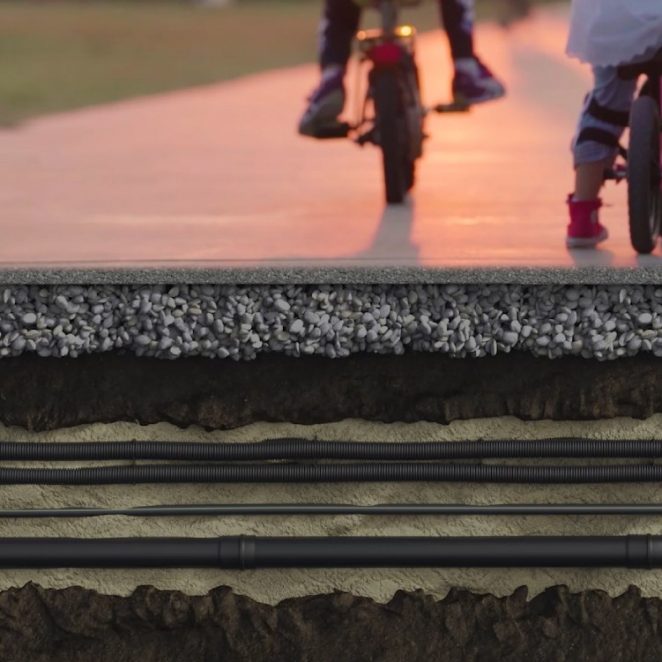 Split view of children riding a bike on a path with cable ducts revealed running underground